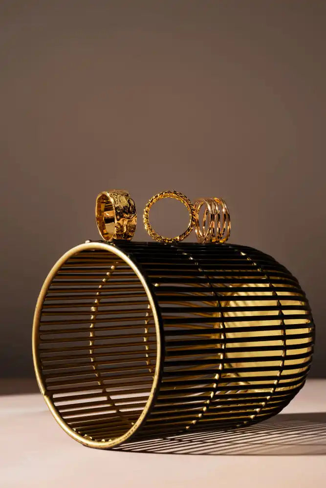 A black and gold cylindrical slatted handbag with three gold rings on top.