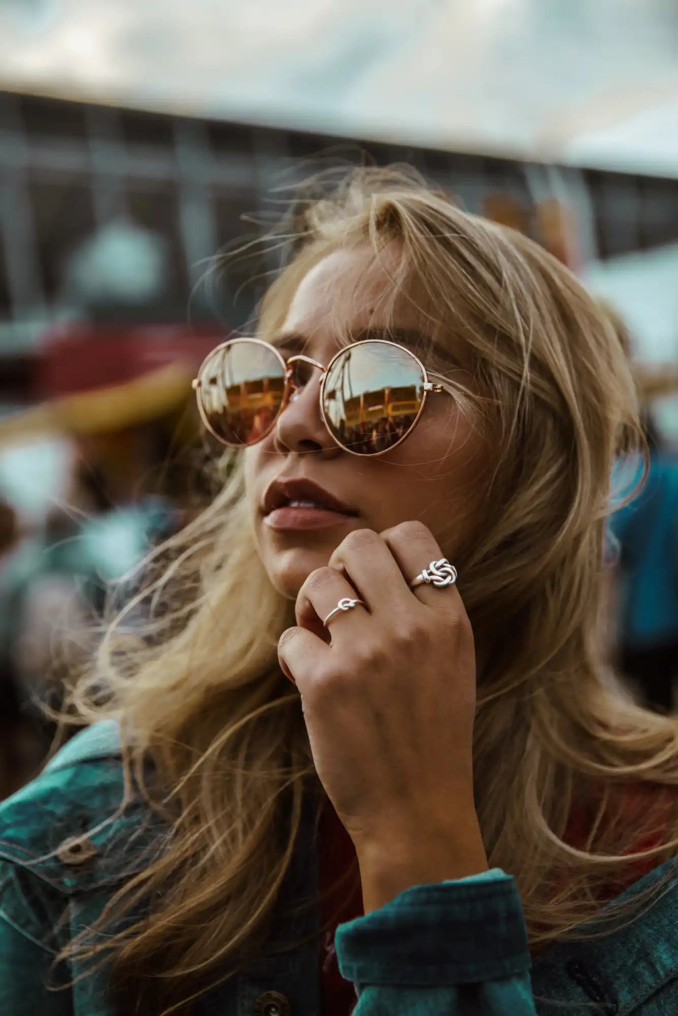 A woman with blonde hair wearing round, reflective sunglasses and two rings on her right hand.