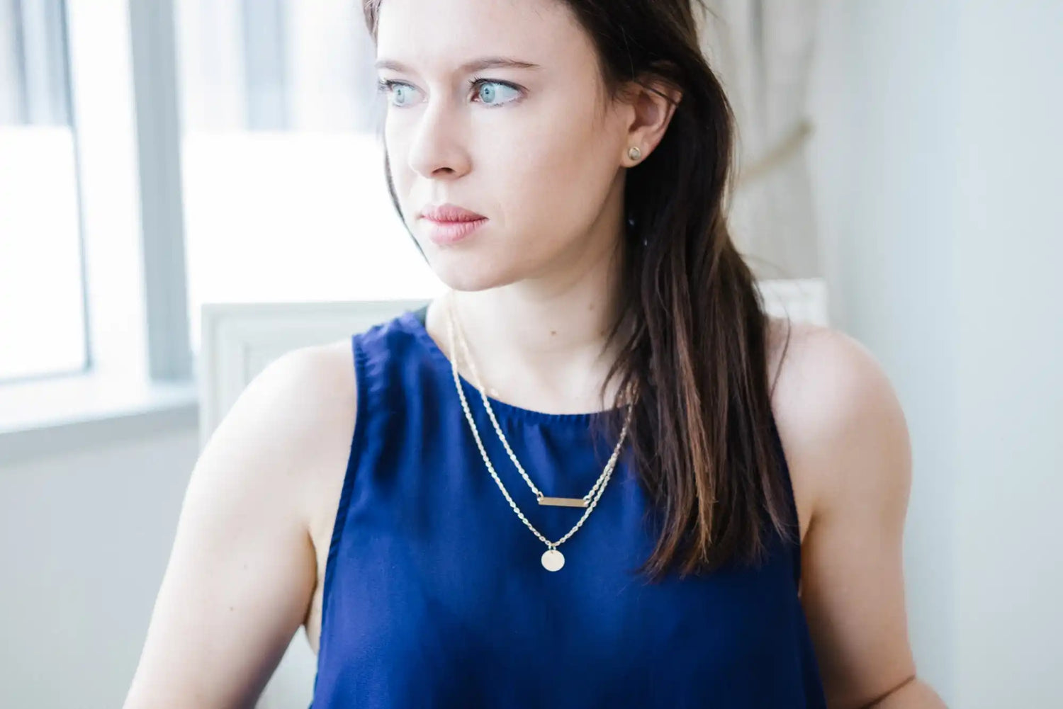 A woman wearing a dark blue top and two silver layered necklaces.